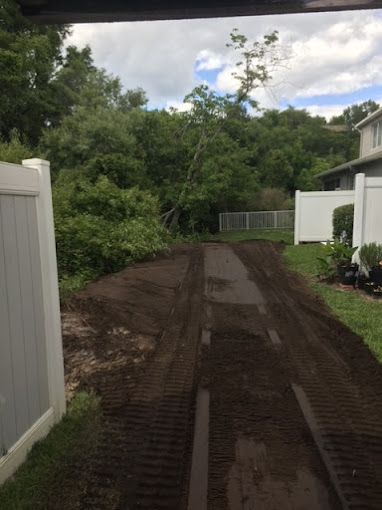 A dirt road leading to a house with a white fence.