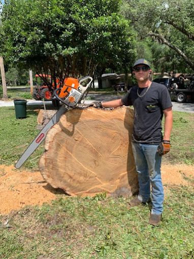 A man is standing next to a large tree stump with a chainsaw.