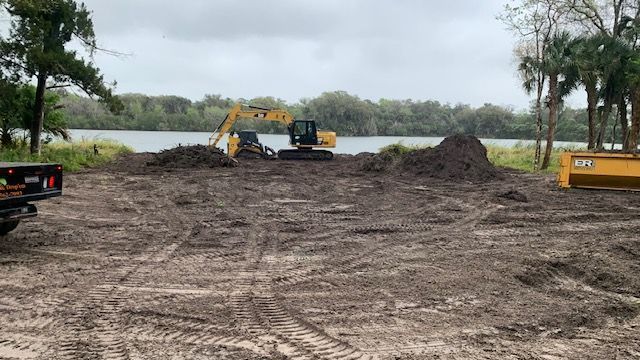 Cleared land with excavator and equipment near a lake, ready for grading or development.