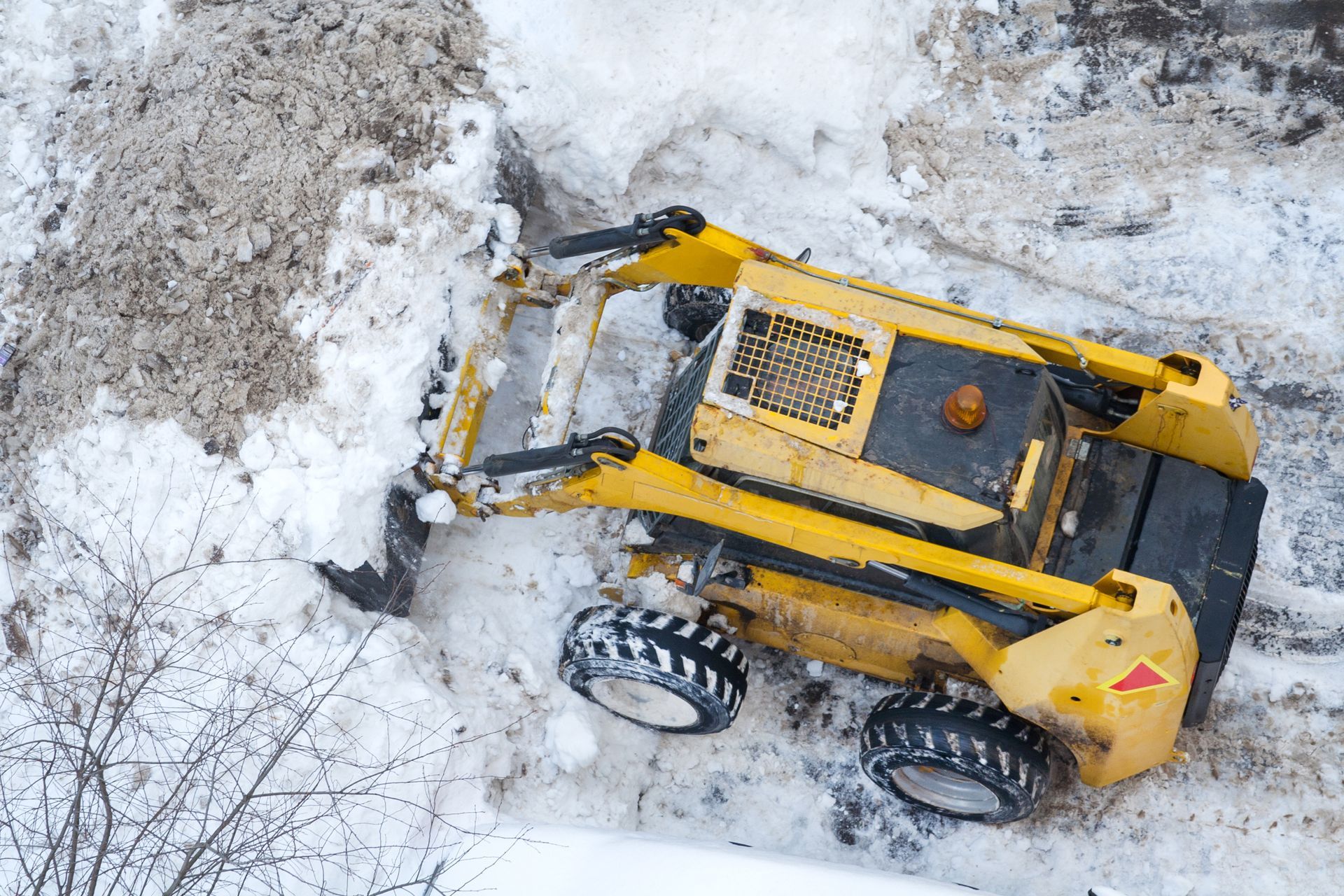 An aerial view of a yellow snow plow clearing snow from a road.
