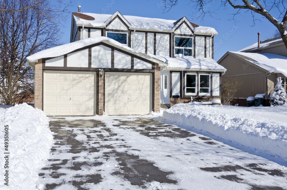 A house with two garage doors is covered in snow.