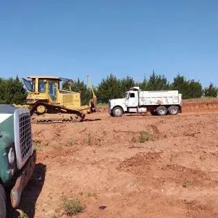 A bulldozer and dump truck work on a construction site under a blue sky.