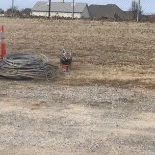Coils of silver wire and orange construction cone on a dirt field with houses in the background.