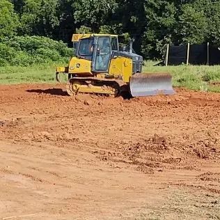 Yellow bulldozer leveling red dirt in a field.