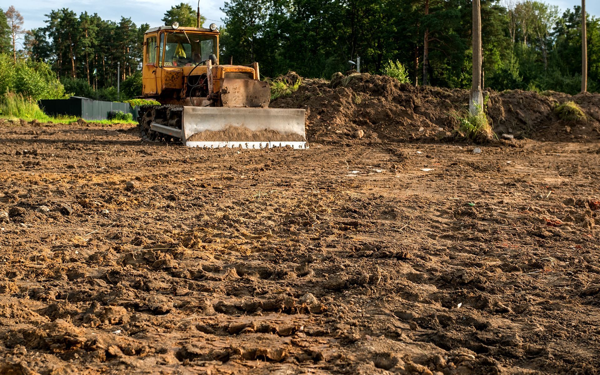 Yellow bulldozer leveling dirt in a field, preparing for construction.