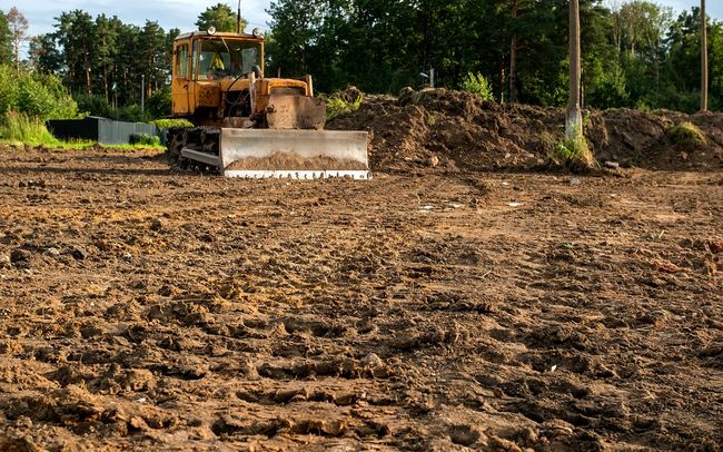 Yellow bulldozer leveling dirt in a field, preparing for construction.