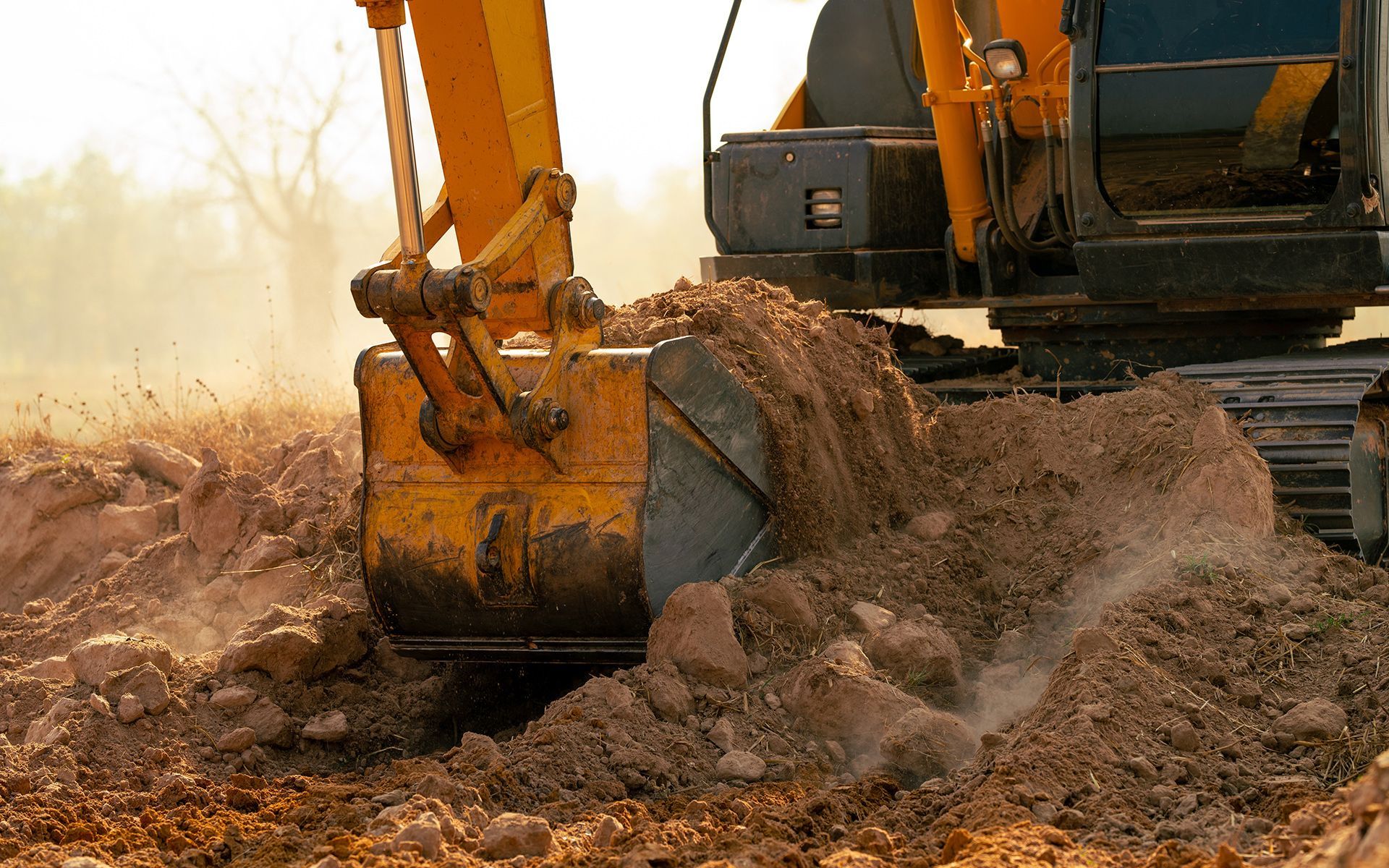 Excavator bucket dumping soil onto the ground during earthwork. Yellow machinery against an overcast backdrop.