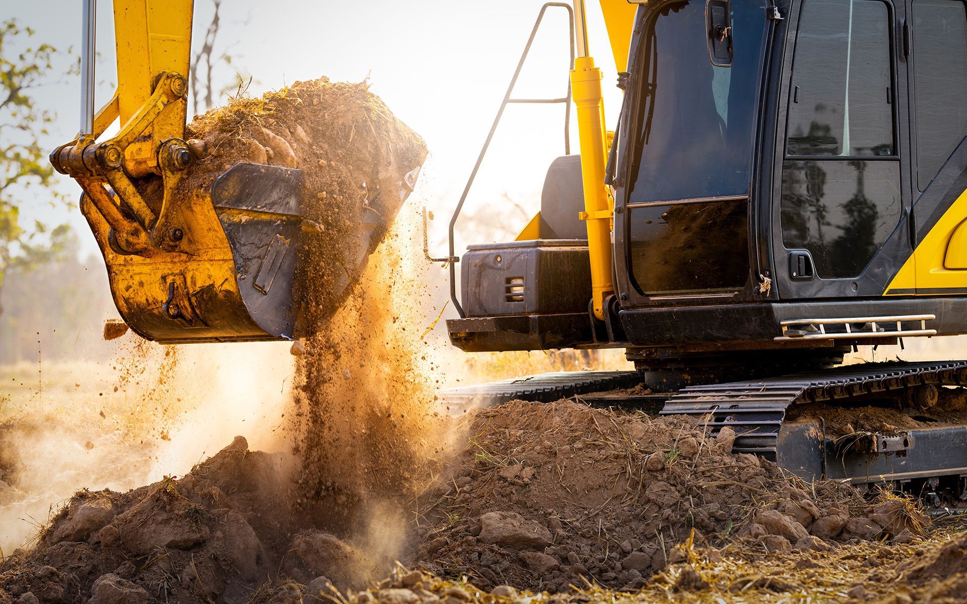 Yellow excavator dumping dirt on a sunny construction site.