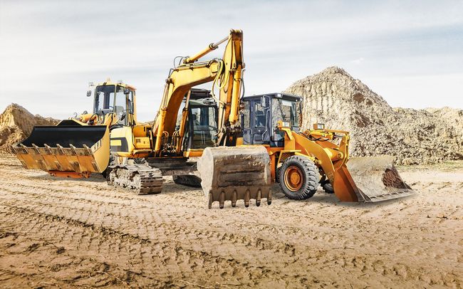 Yellow construction vehicles on a dirt field: excavator, backhoe, and front-end loader near a pile of dirt.