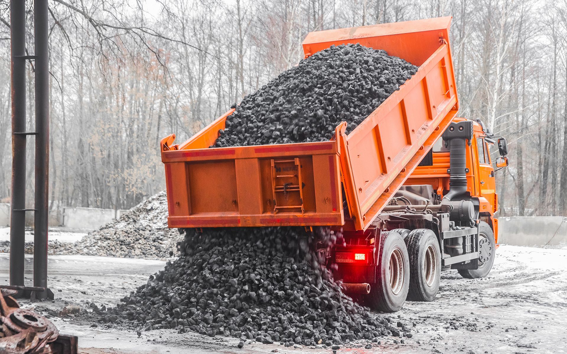 Orange dump truck unloading a pile of dark grey coal onto snowy ground.