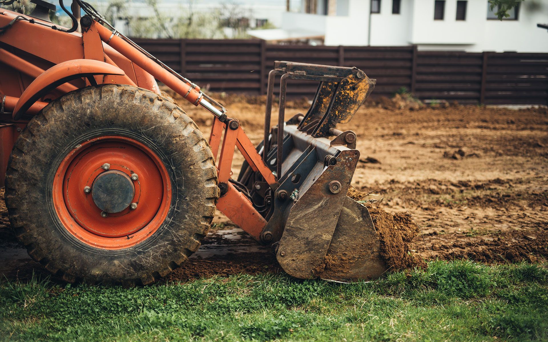 Red tractor with scoop digging into dirt, preparing ground.