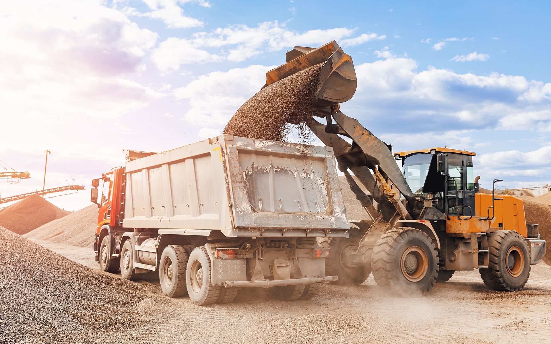 Yellow loader dumping gravel into a red dump truck at a construction site.