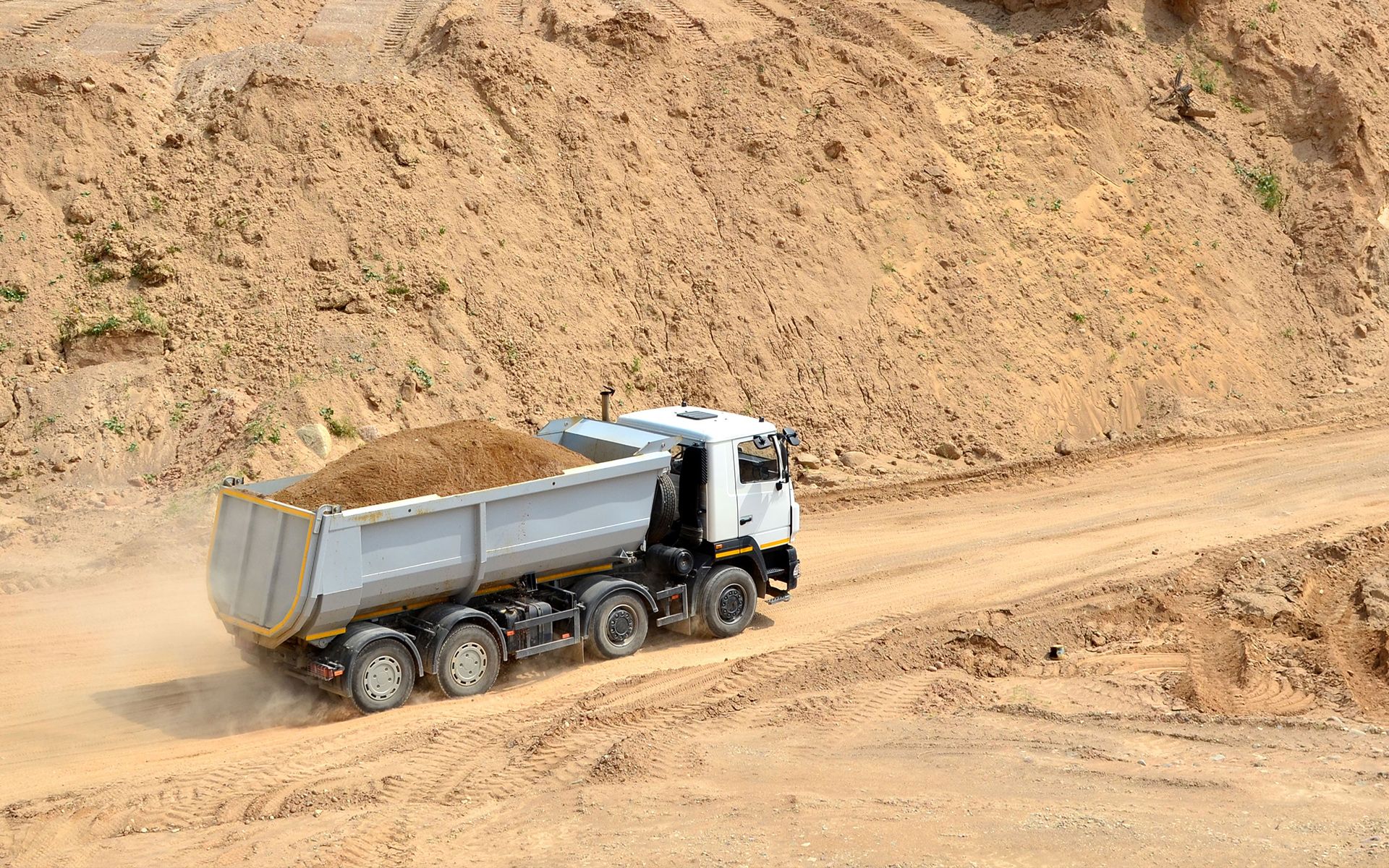Dump truck hauling sand on a dirt road near a large sand pile.