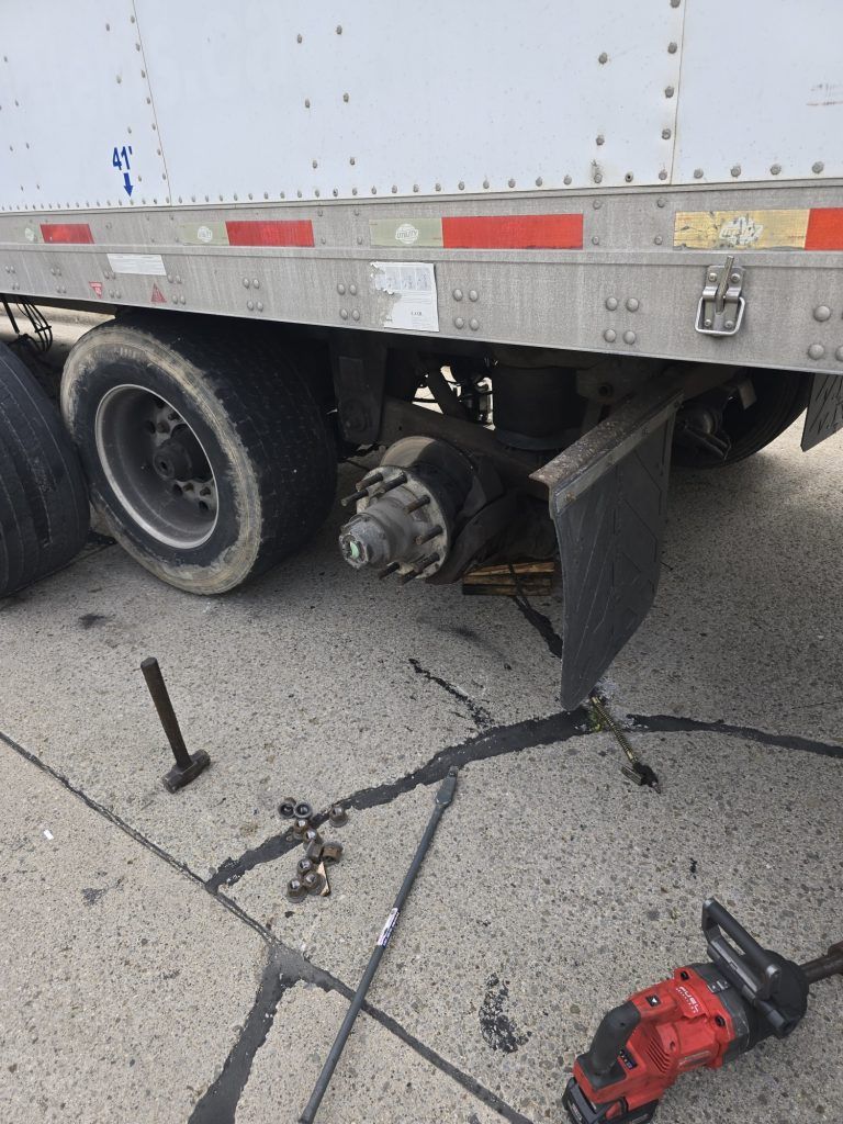 A semi truck with a broken axle is sitting on the side of the road.