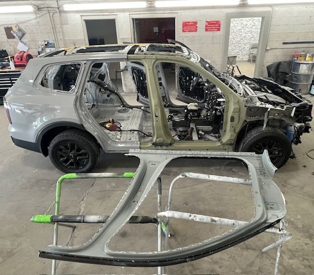 SUV undergoing body repair work in a garage, with a door panel in the foreground.