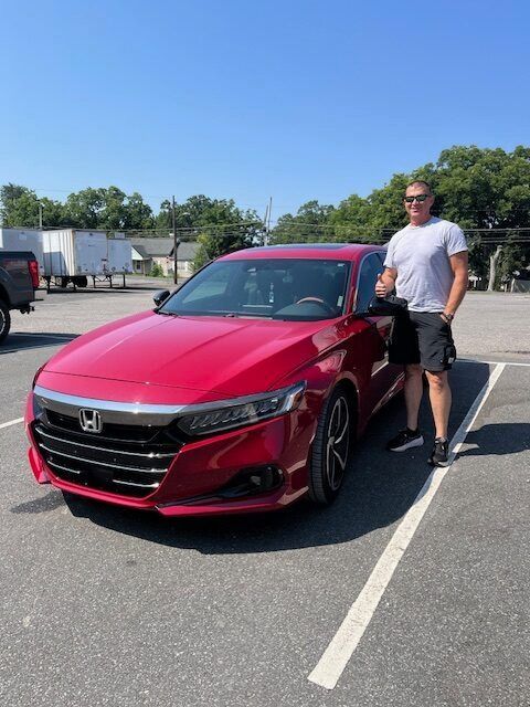 Man standing next to a red Honda Accord in a parking lot on a sunny day. He gives a thumbs-up.