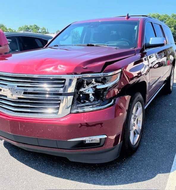 Red SUV with front-end damage. In a parking lot on a sunny day.