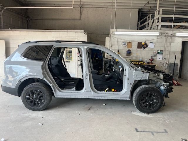 Gray SUV undergoing repairs in a garage, doors removed, revealing interior and exposed frame. Black wheels.