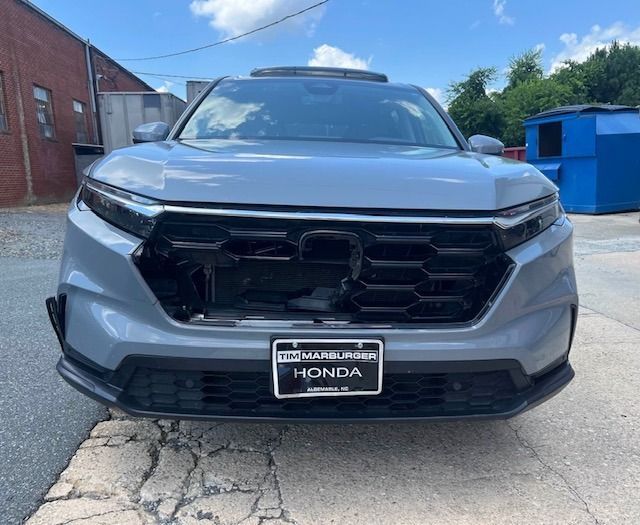 Gray Honda SUV with damaged front grille, parked outside a brick building.
