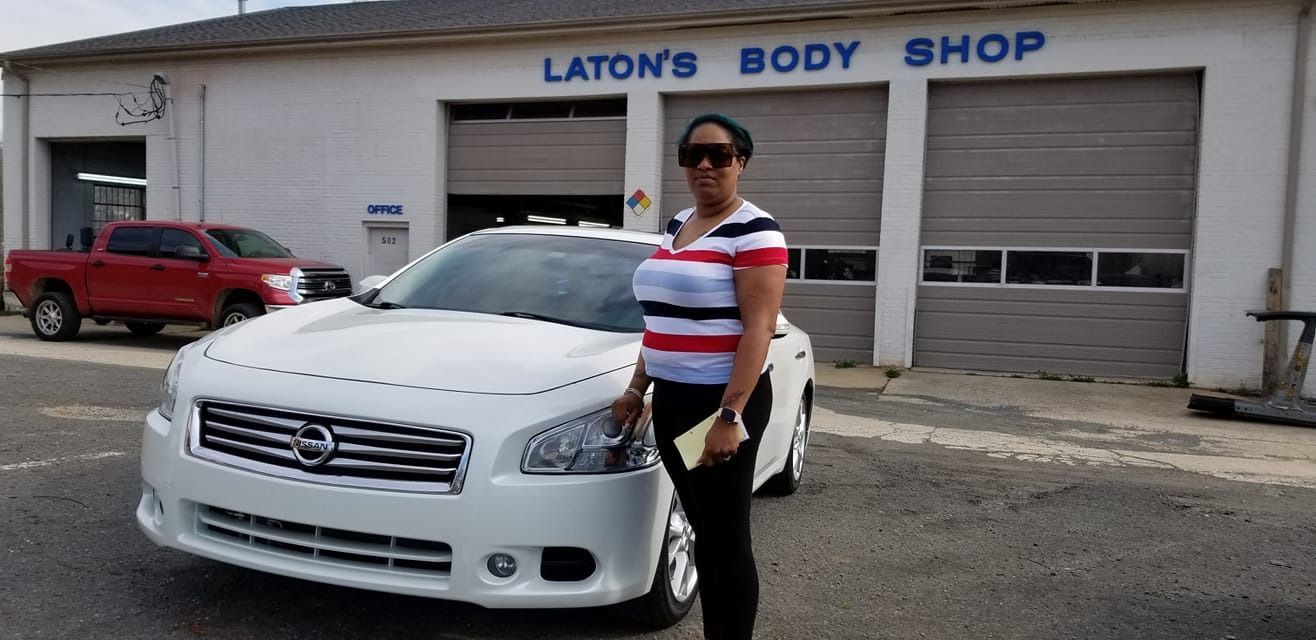 Woman standing beside a white car in front of Laton's Body Shop, red pickup truck in the background.