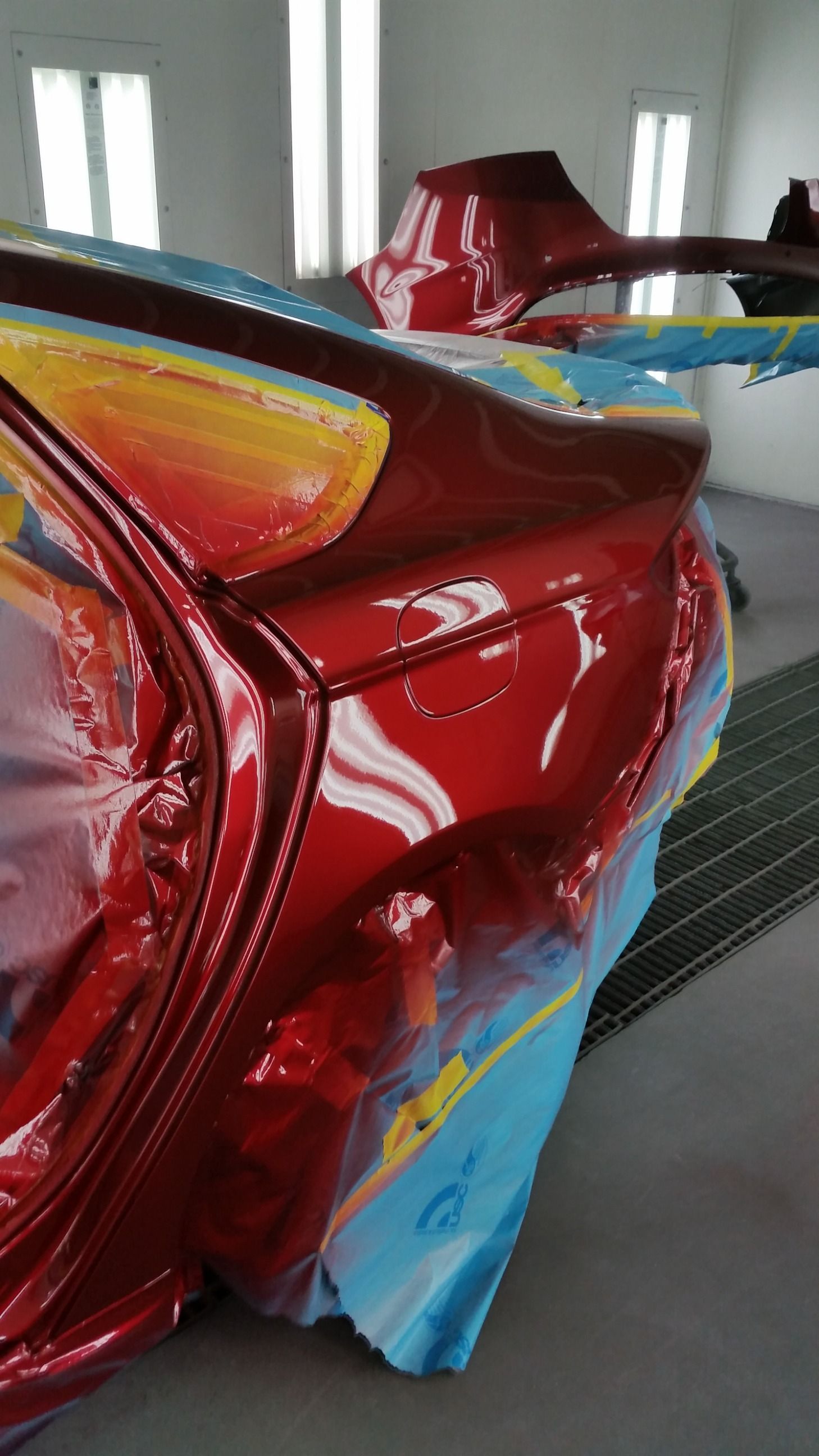 Close-up of a red car body, with a glossy finish, being painted. Detail of rear side in a paint booth.