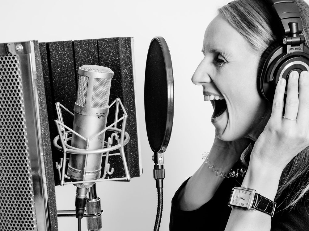 Frau singt mit Kopfhörern in ein Studiomikrofon und blickt auf einen Popfilter.