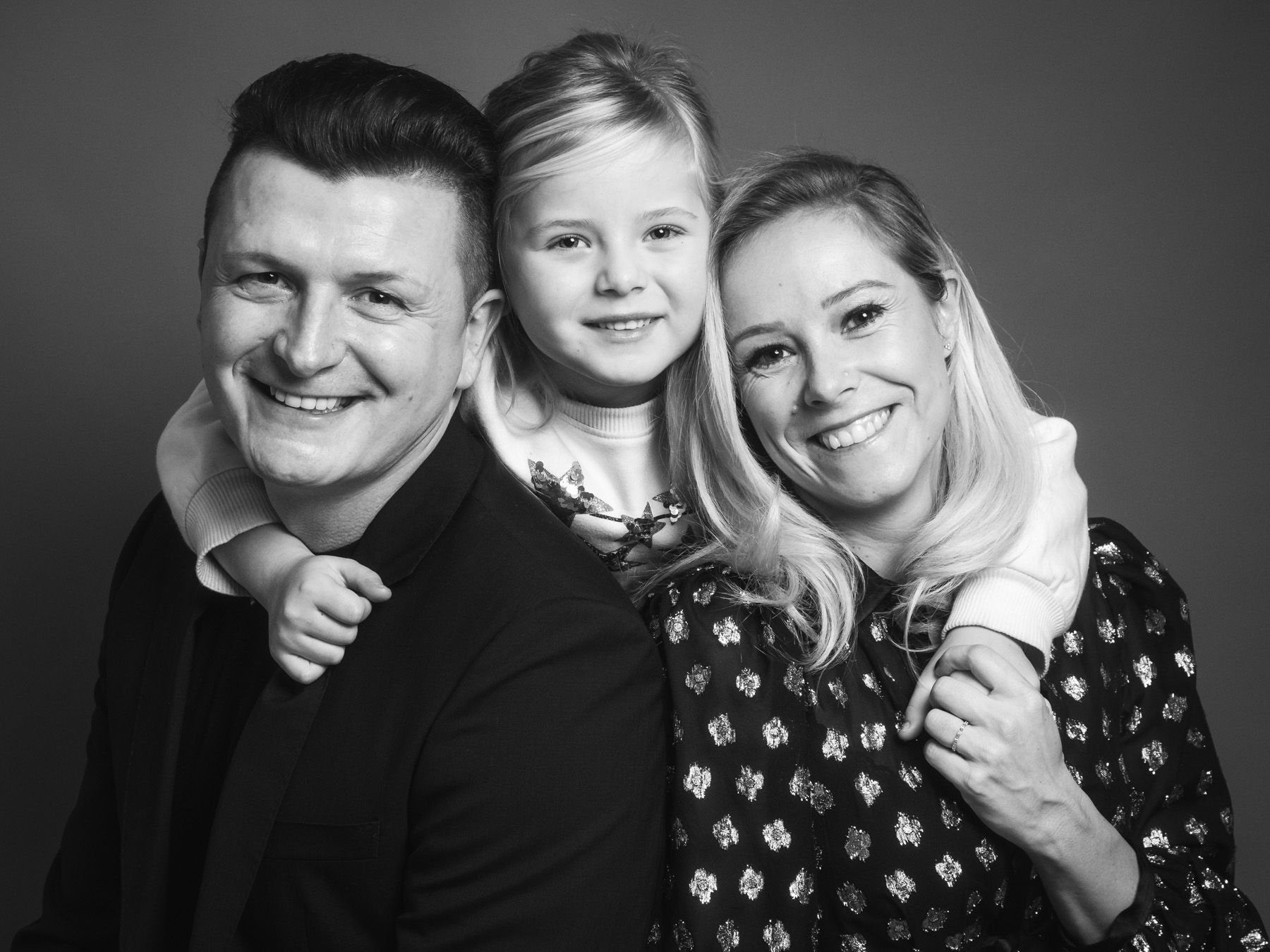Eine lächelnde dreiköpfige Familie posiert eng in einem Schwarz-Weiß-Porträt.