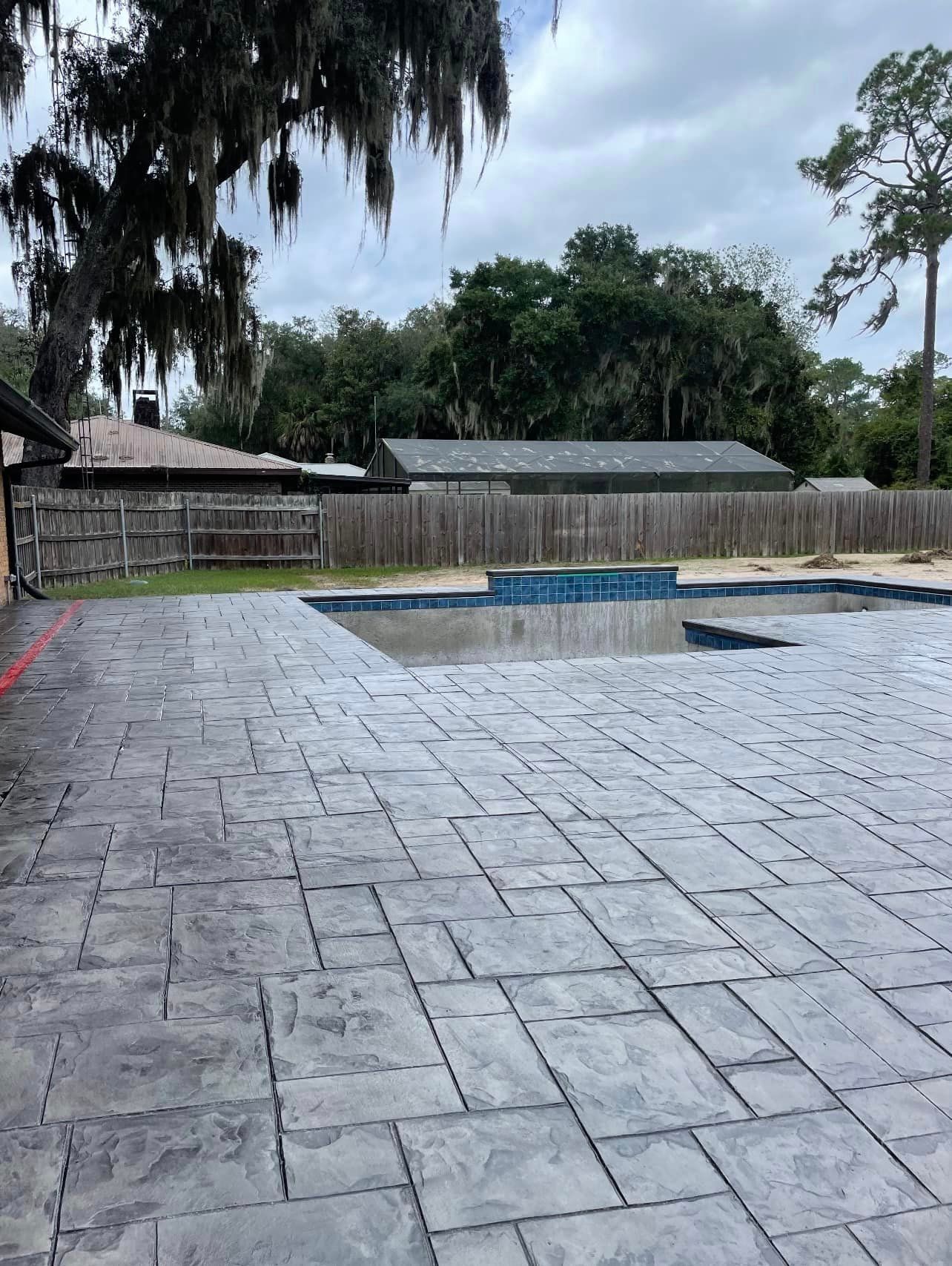 A large concrete patio with a pool in the background.
