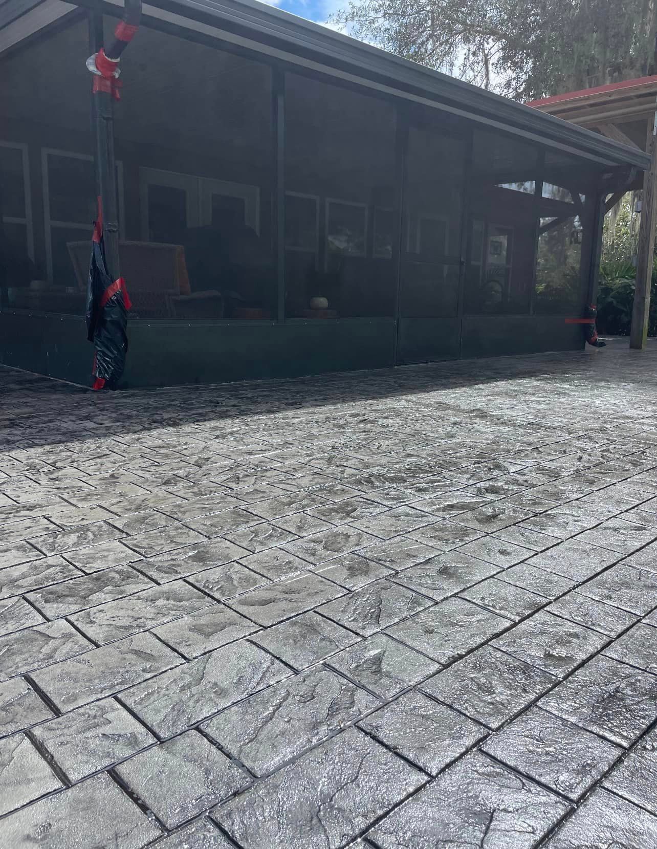 A brick driveway in front of a house with a screened in porch.