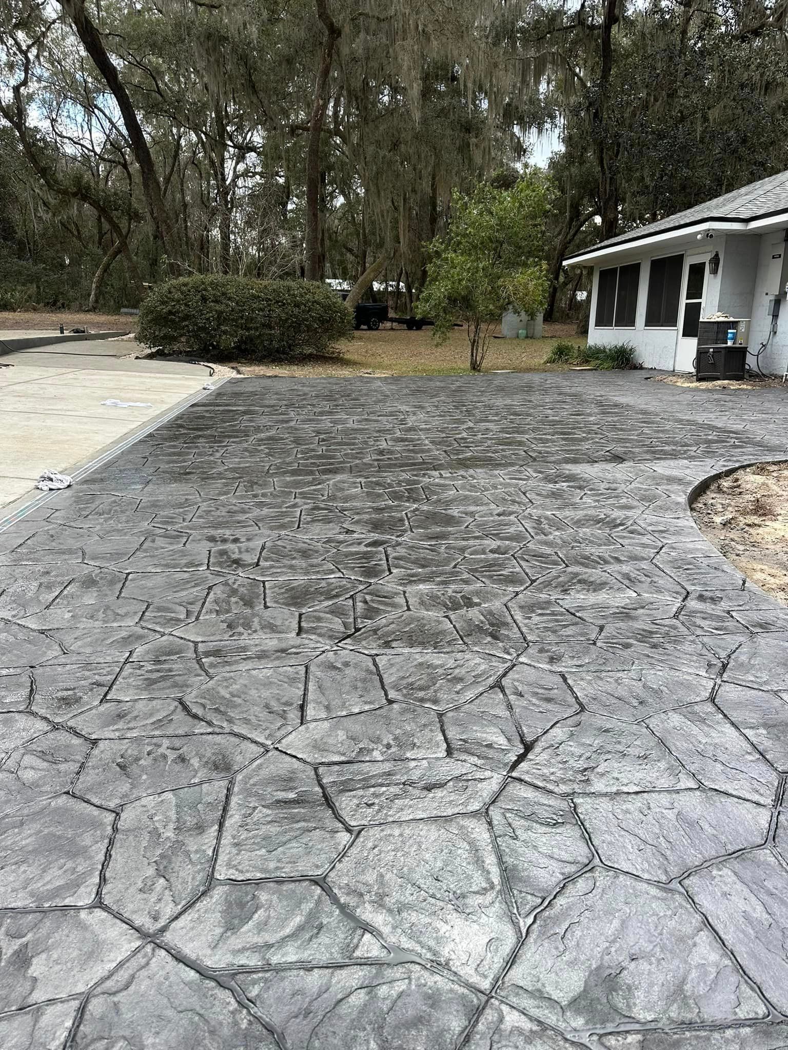 A concrete driveway leading to a house with trees in the background.