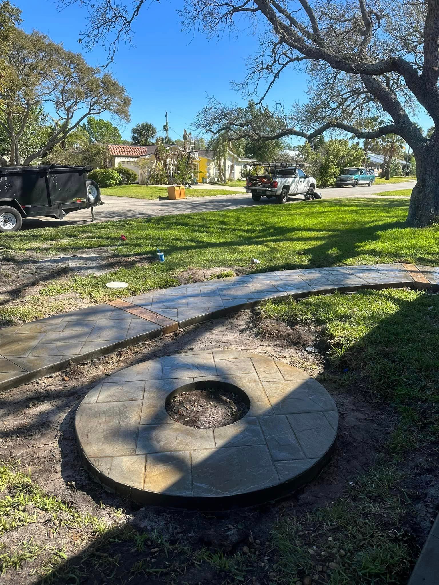 A fire pit is sitting in the middle of a lush green field next to a sidewalk.