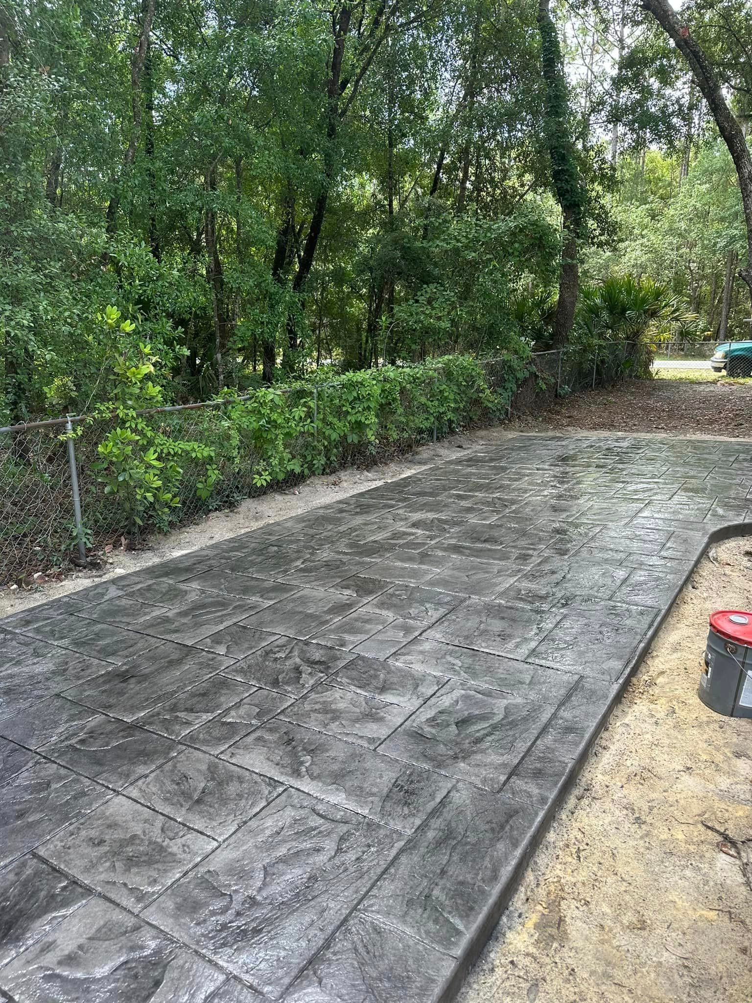 A concrete driveway with a fence and trees in the background.