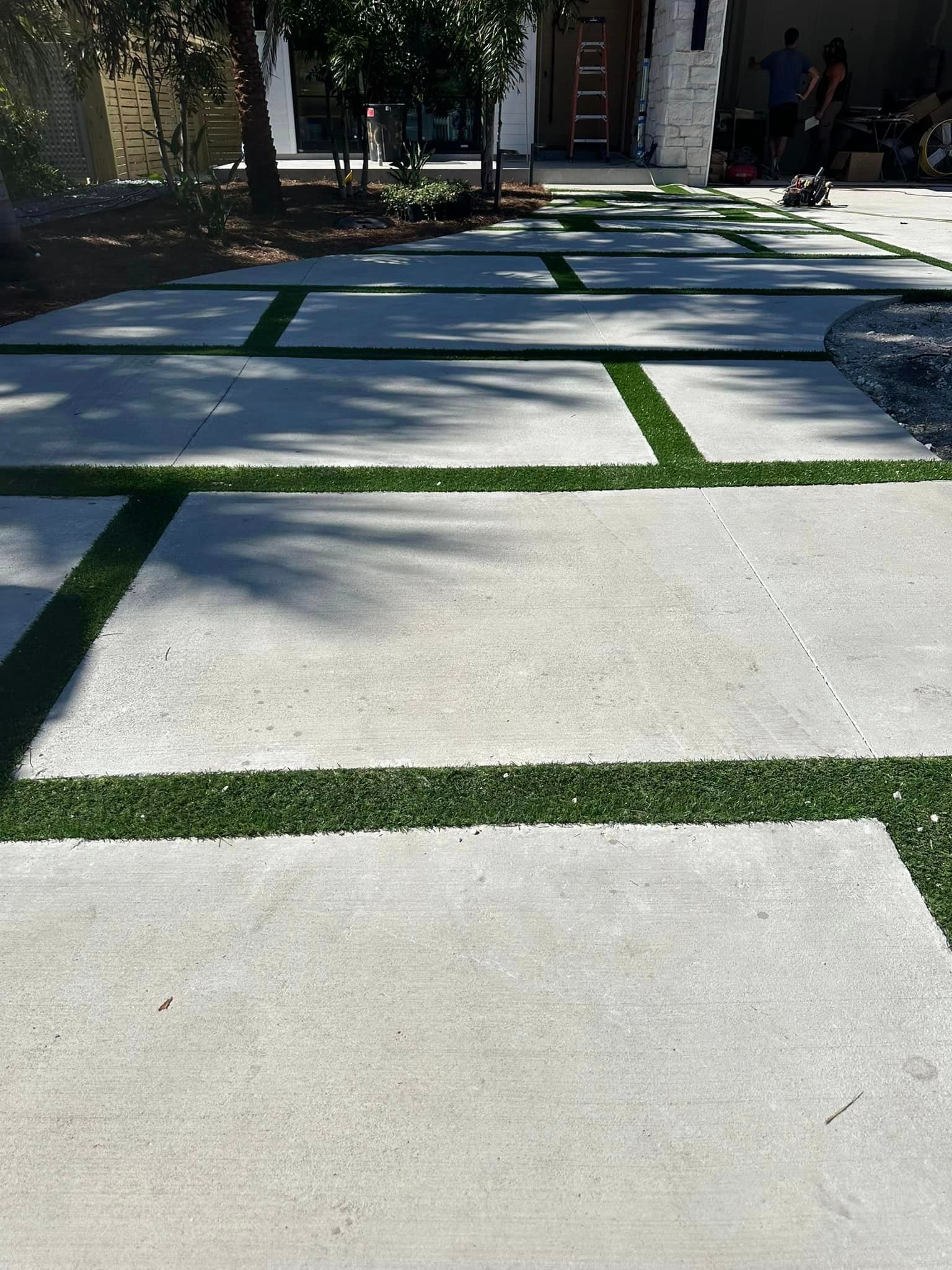 A concrete driveway with artificial grass in the middle of it.