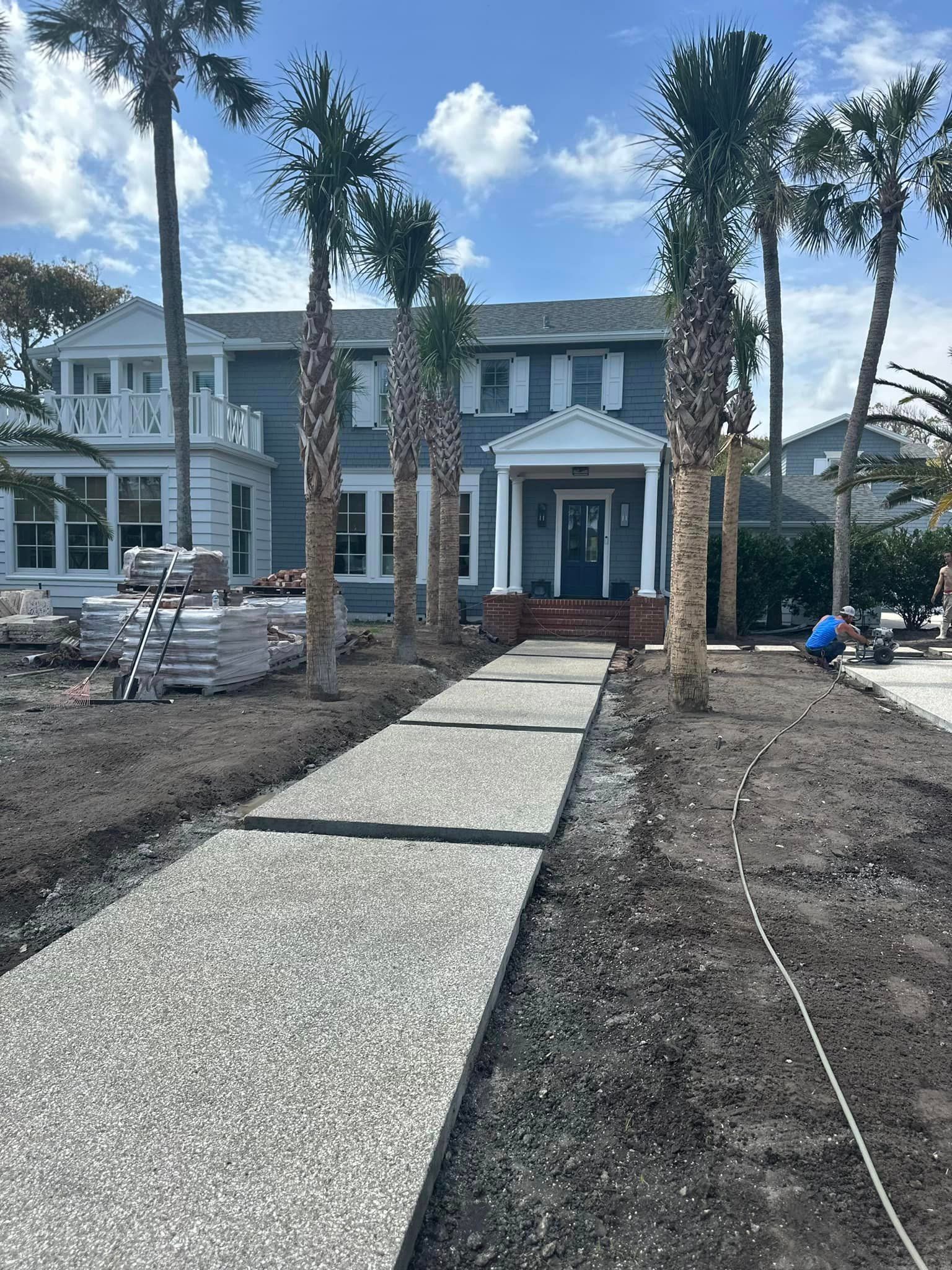 A concrete walkway is being built in front of a house with palm trees.