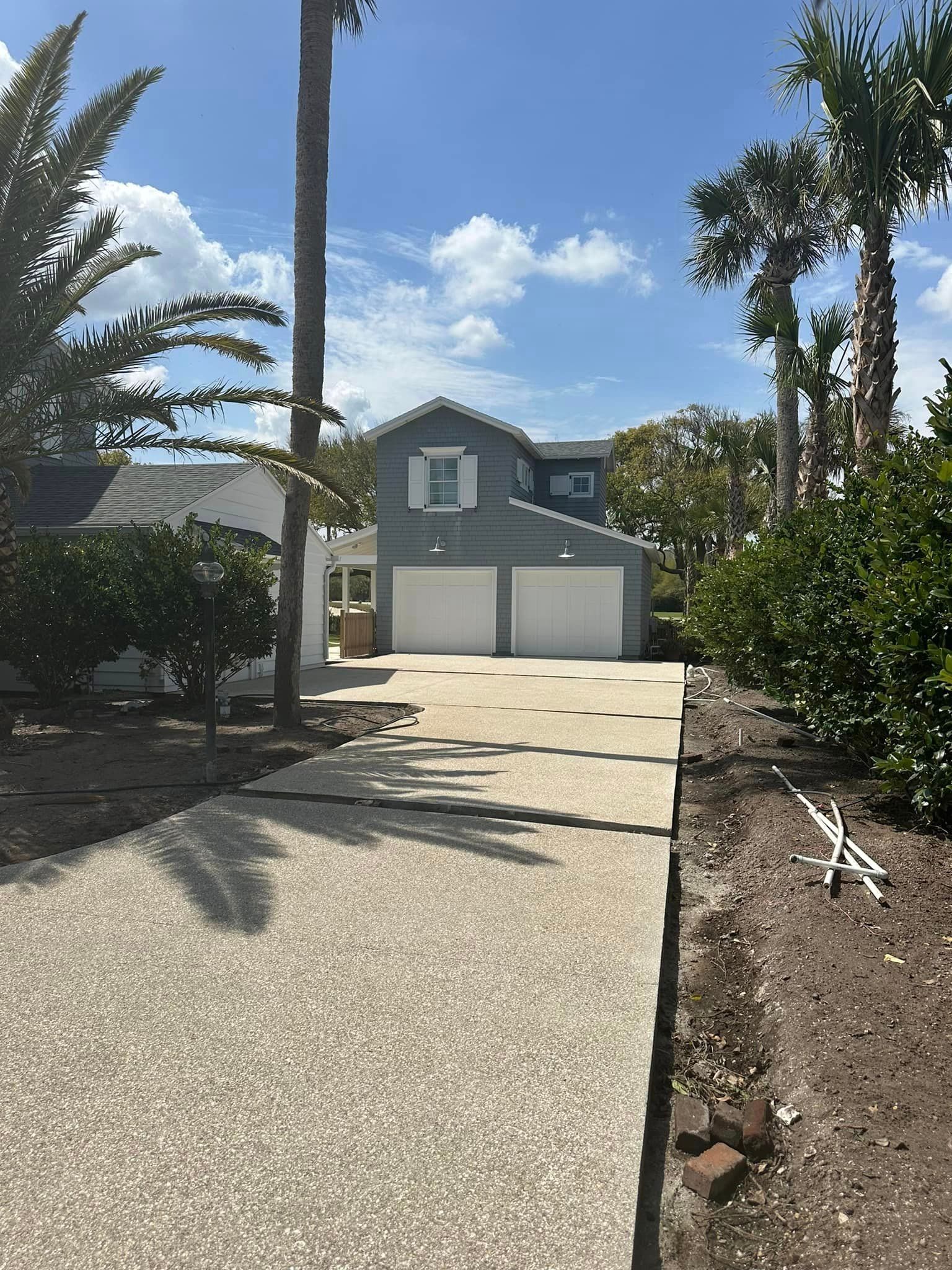 A driveway leading to a house with two garages and palm trees.