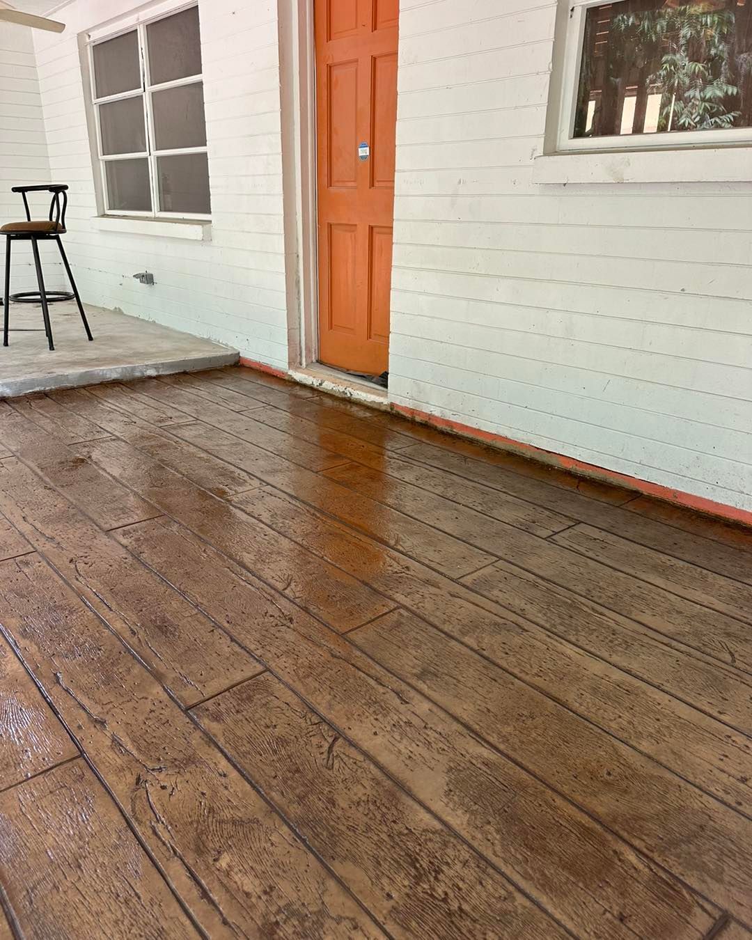 A porch with a wooden floor and an orange door