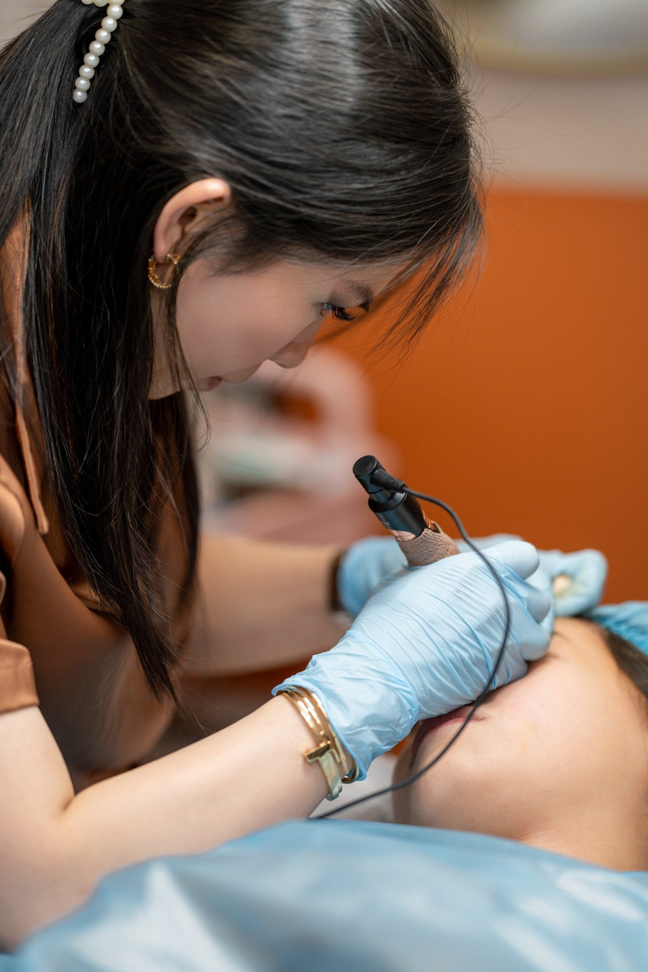 Technician performing cosmetic eyebrow procedure on a client, using a handheld device.