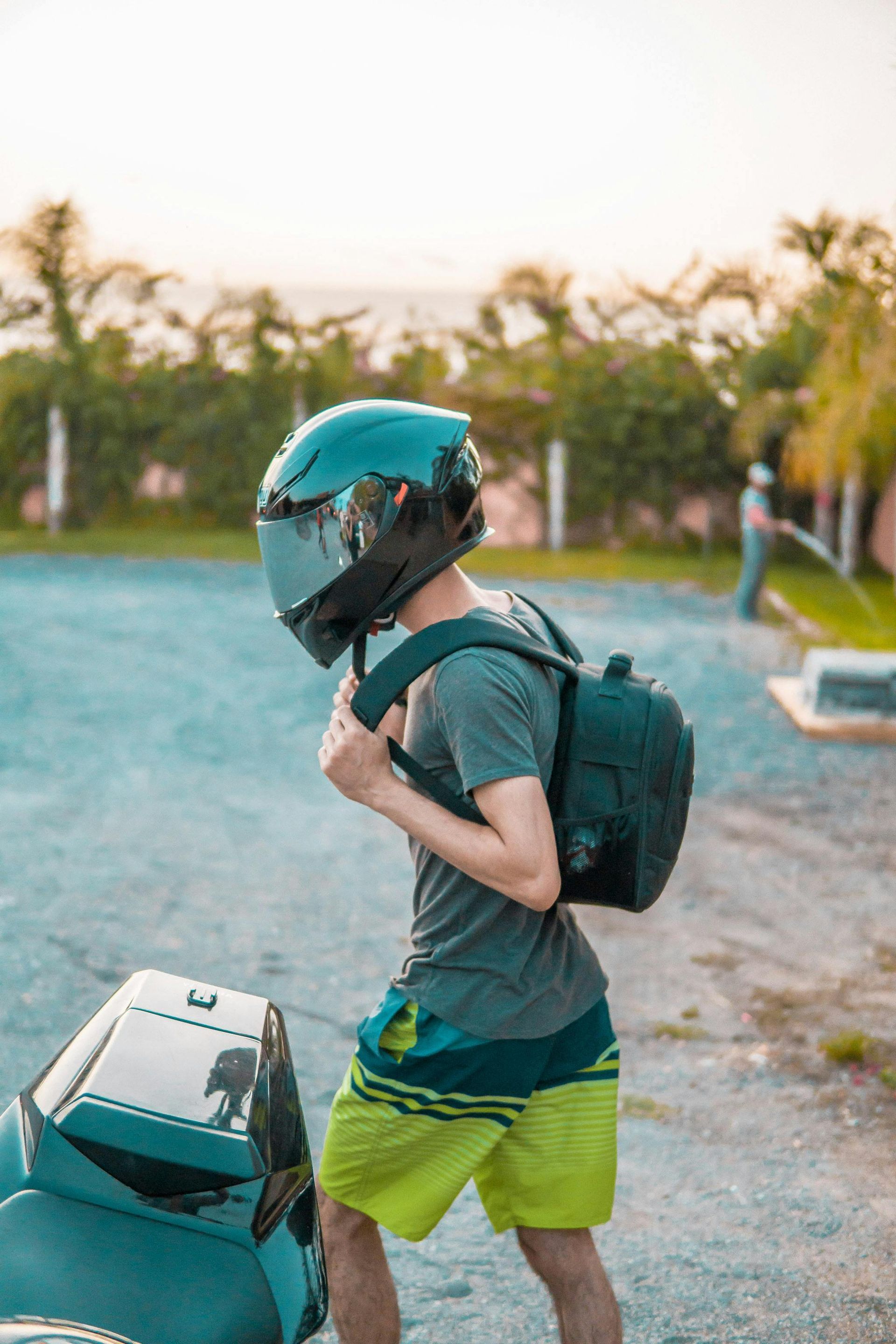 A man wearing a helmet and a backpack is standing next to a motorcycle.