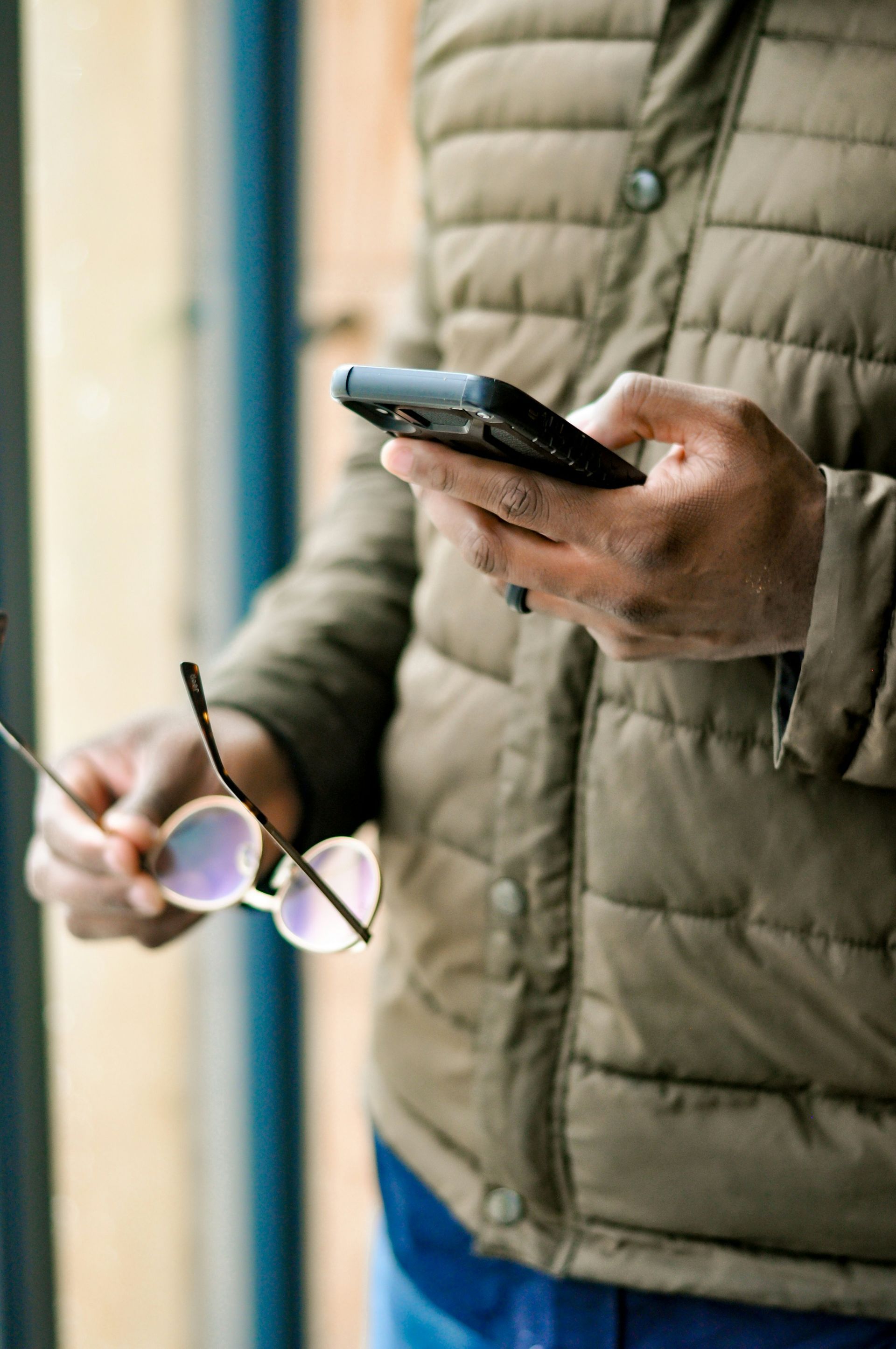 A person is holding a pair of sunglasses and a cell phone.
