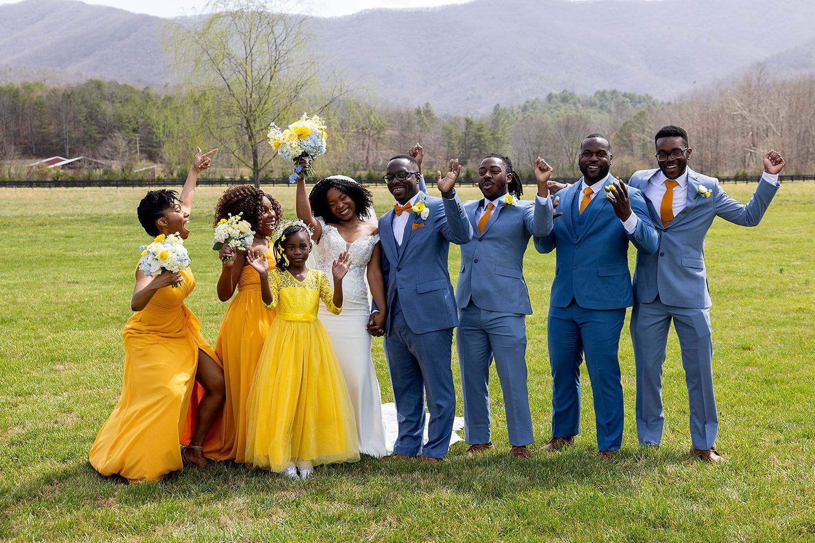 A bride and groom are posing for a picture with their wedding party in a field.