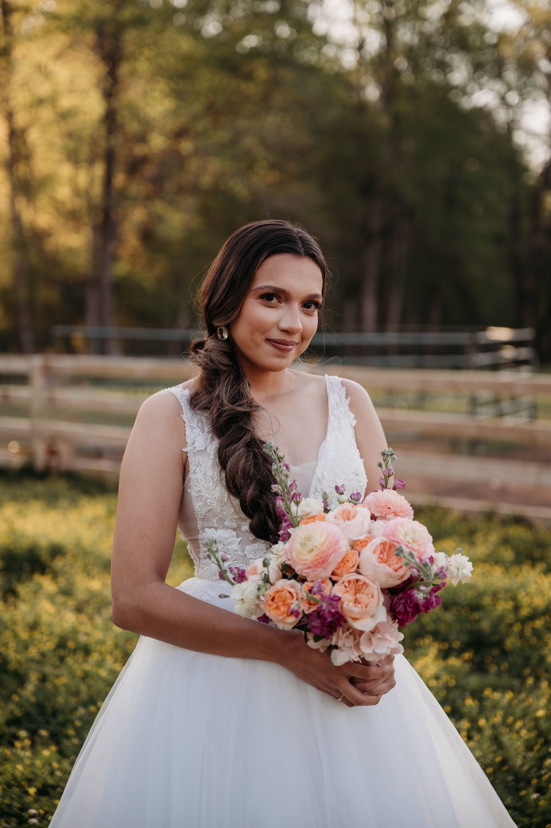 A bride in a white dress is holding a bouquet of flowers in a field.