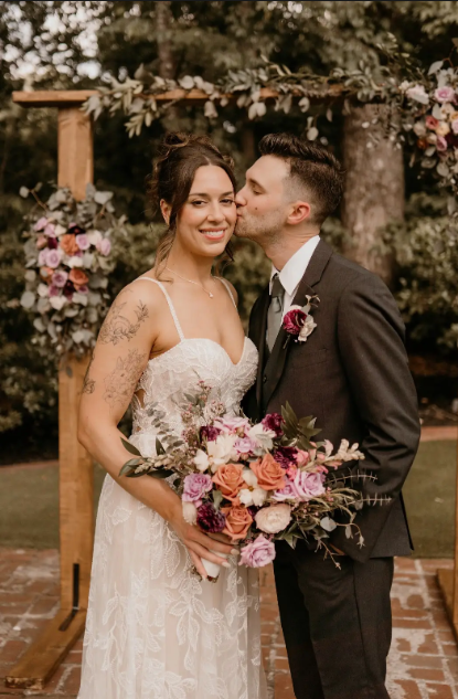 A bride and groom are kissing in front of a wooden arch.