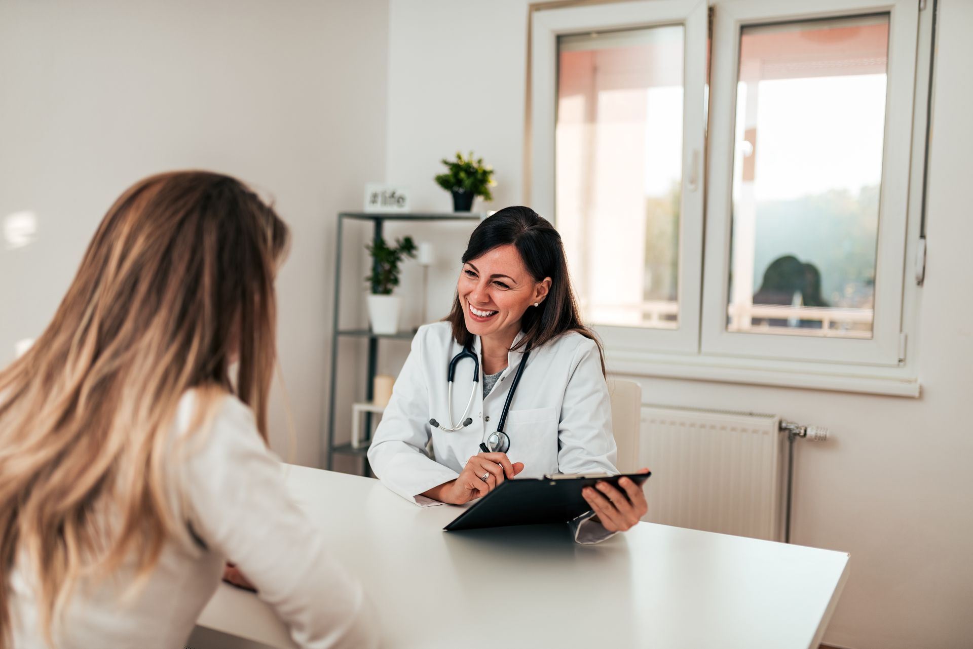 A healthcare provider consults with a patient at a desk in a bright, modern medical office. A healthcare provider consults with a patient at a desk in a bright, modern medical office.
