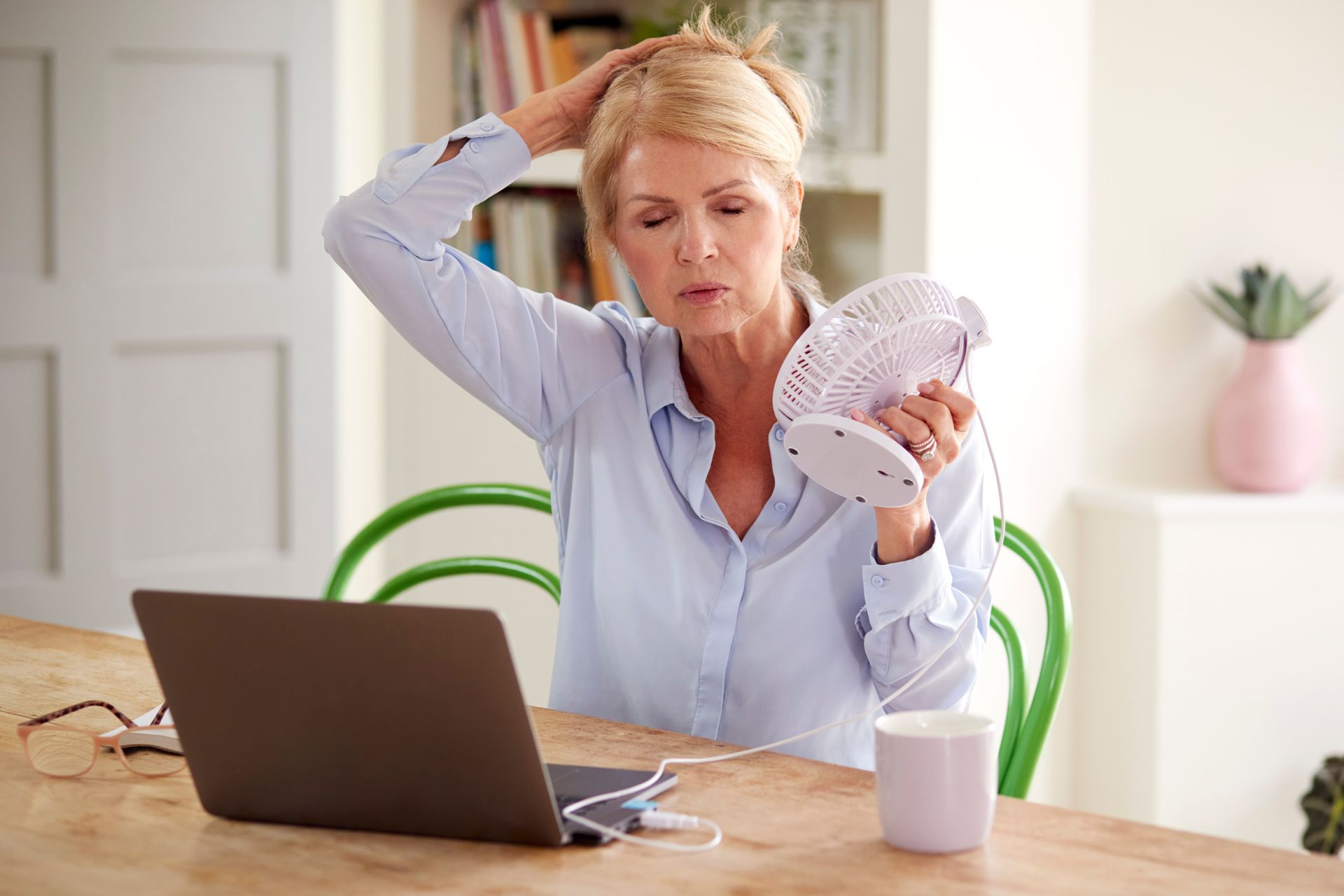 A woman with menopause is cooling herself with a fan.