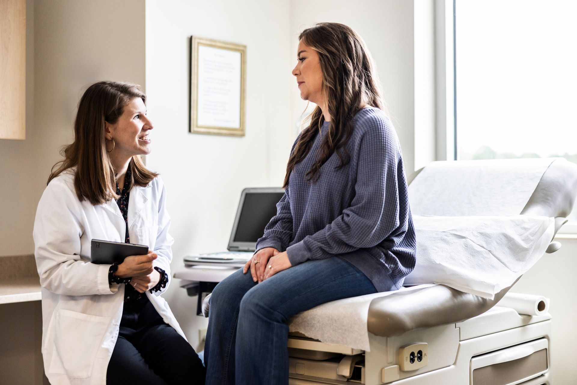 Female doctor consulting patient sitting on exam table at modern women’s health clinic.