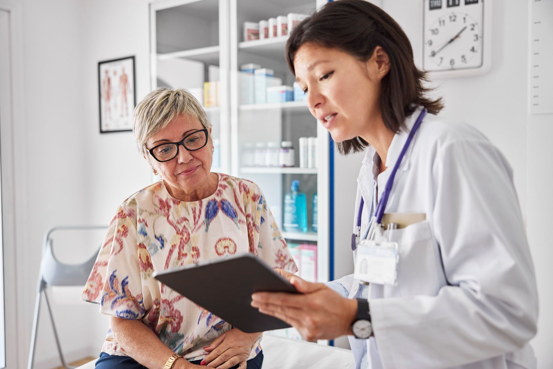 Female doctor consulting mature woman at modern women’s health clinic using digital tablet.