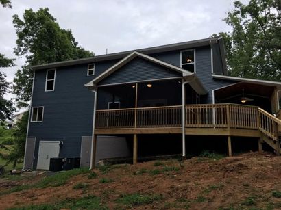 Two-story dark blue house with a wooden deck on a wooded hillside