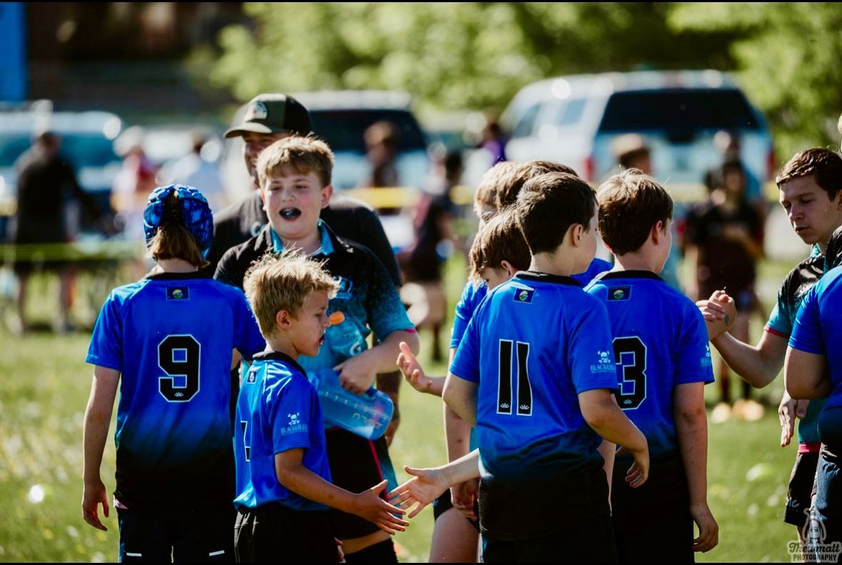 Youth rugby team in blue jerseys on a field; boys smiling, high-fiving, and talking.