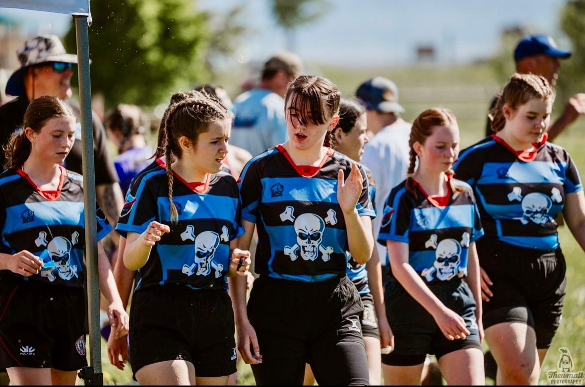 Group of young female athletes in skull jerseys walking on a field.
