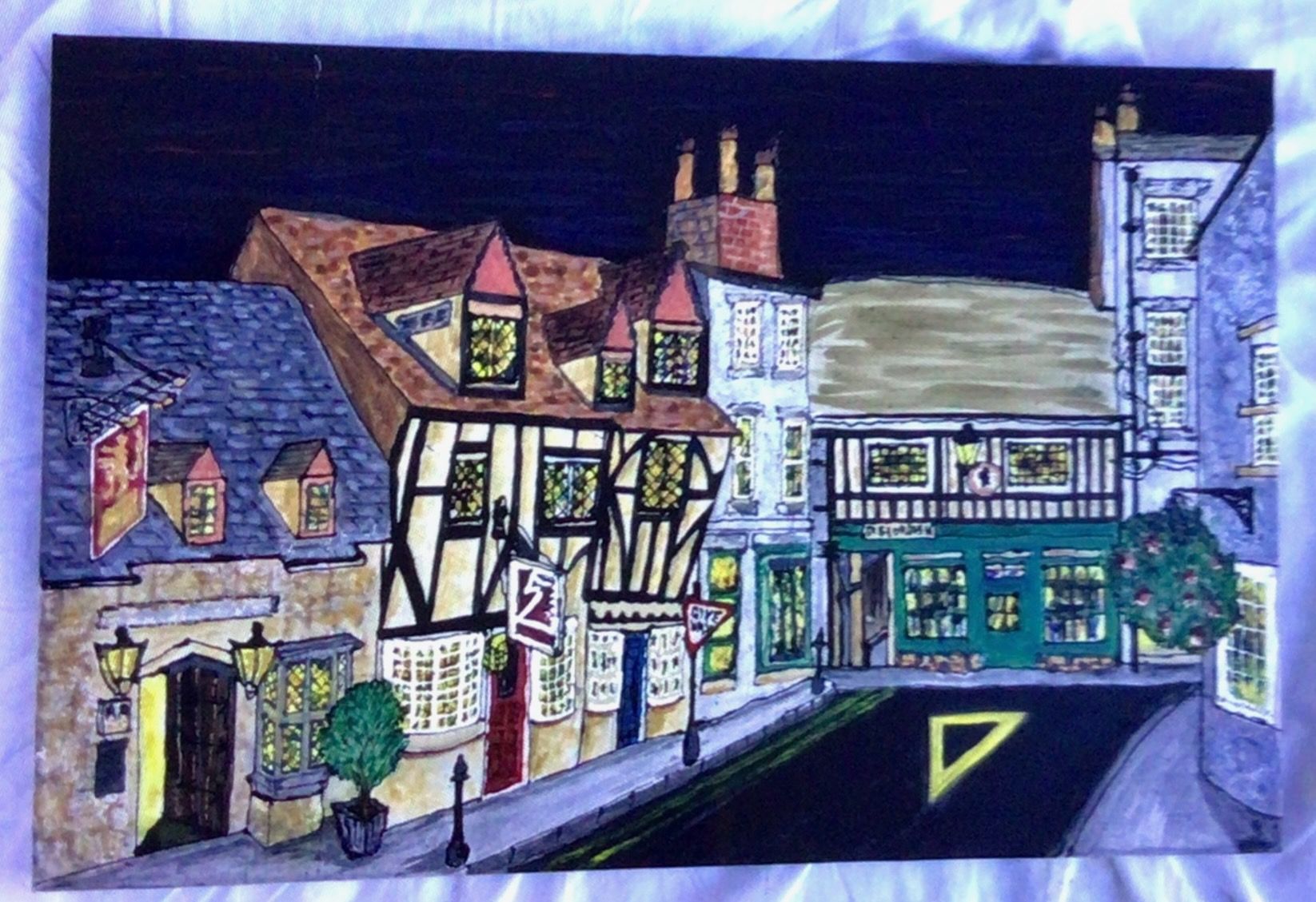 Town street scene with half-timbered buildings, lit windows, a road, and a dark, starry sky.